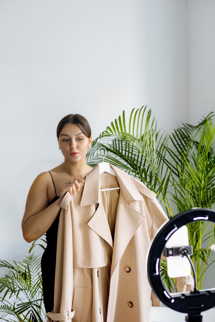 gallery-2 A fashion vlogger presents a chic beige coat during an indoor recording session with ring light.
