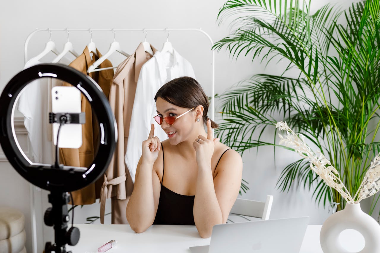 hero-img-01 Stylish woman vlogging with ring light, surrounded by fashion accessories and greenery.