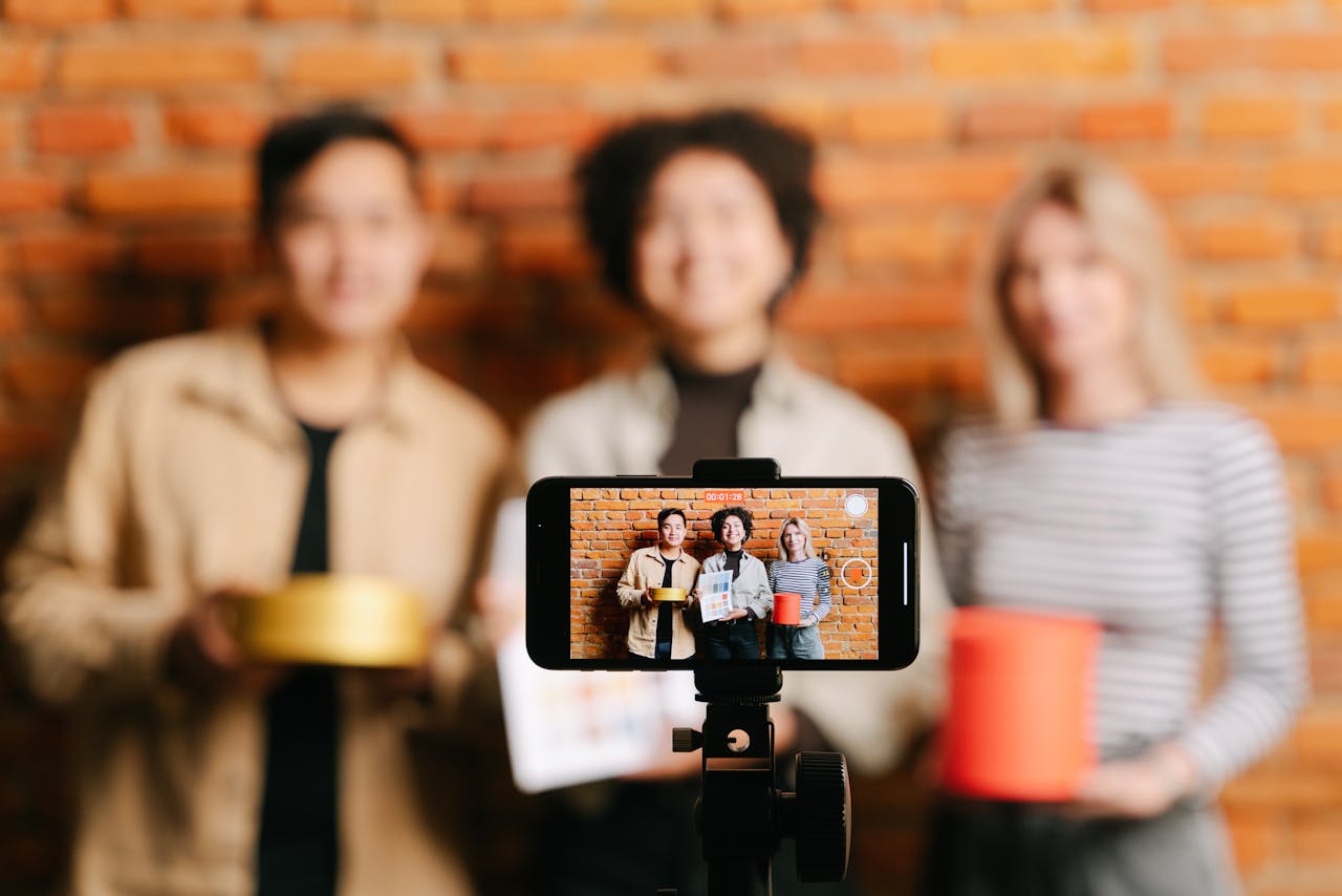 hero-img-02 A diverse team of vloggers recording a video with a smartphone against a brick wall backdrop.