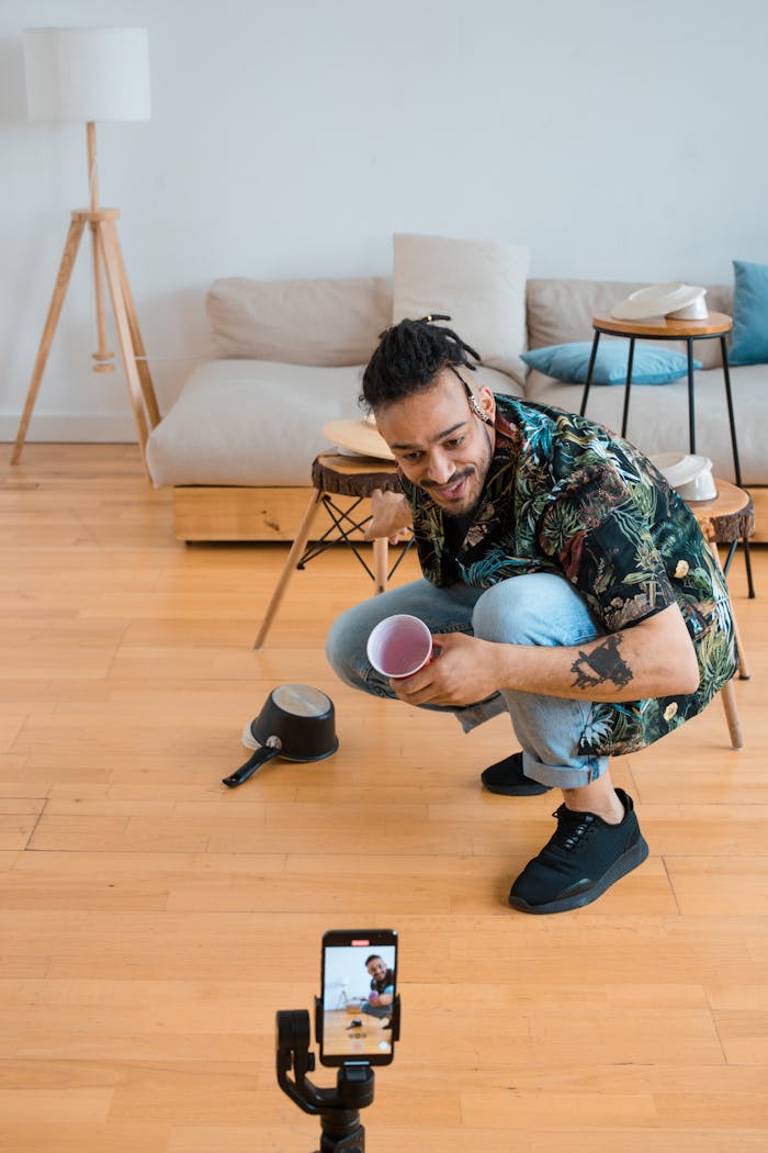 gallery-6 A young man squatting indoors, filming content using a smartphone in a modern living room.