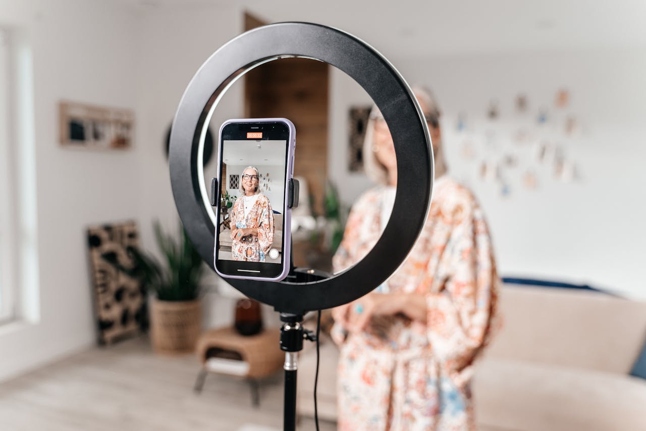 gallery-5 Senior woman creating content at home using smartphone and ring light in a modern setting.